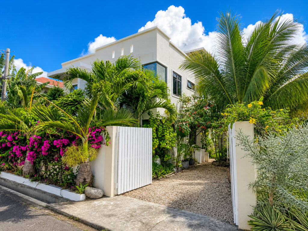 Entrée de Villa Zoli Baz avec jardin tropical, portail blanc et palmiers à La Preneuse