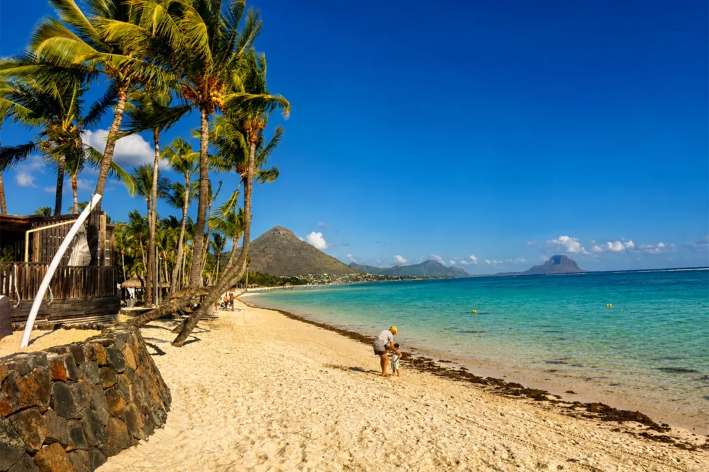 Plage devant un hôtel à Flic en Flac avec cocotier, lagon turquoise, vue sur Le Morne au loin et montagne de La Tourelle