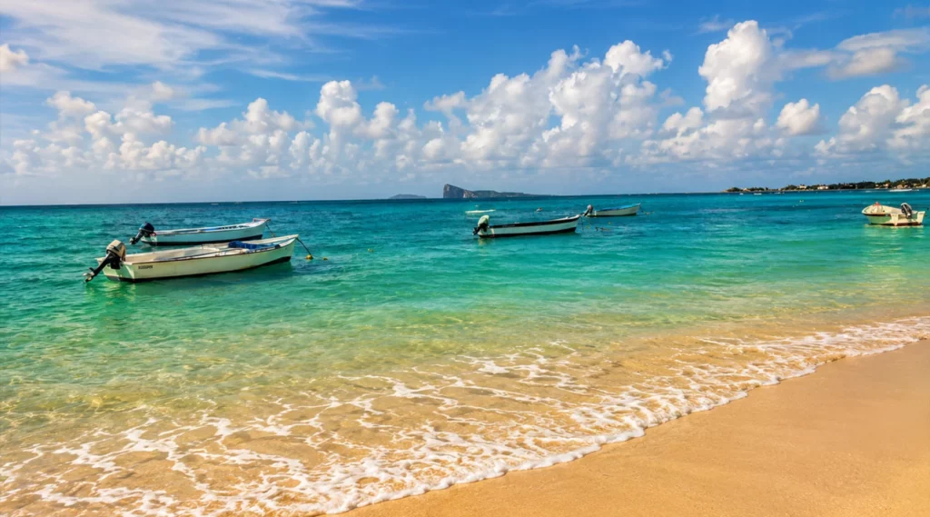 Plage publique du nord de l’île Maurice avec lagon turquoise, bateaux au mouillage et vue sur le Coin de Mire