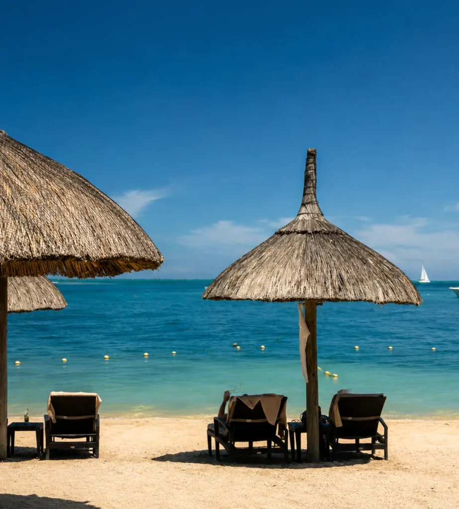 Plage calme à l’île Maurice avec parasols de paille, transats face au lagon turquoise et bateau au loin