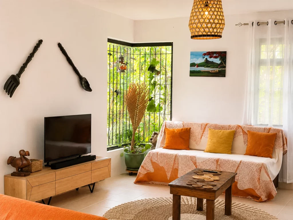 Salon lumineux de la Villa Zoli Baz à La Preneuse avec décoration tropicale, canapé aux tons orangés, plantes vertes et lumière naturelle